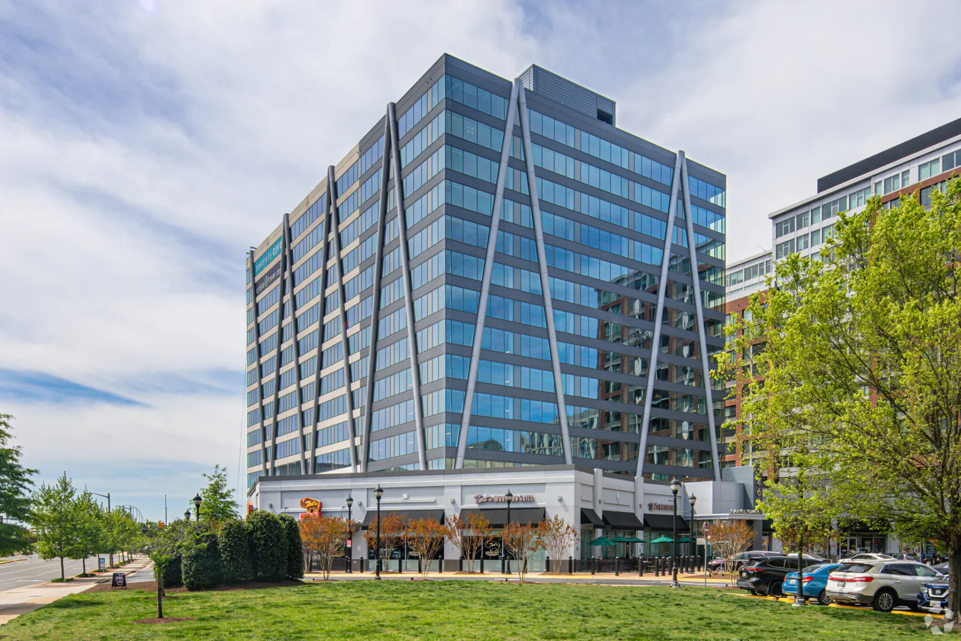 Modern glass office building with crossing diagonal steel supports in a city street setting.